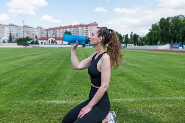 スポーツウーマンはスタジアムで水を飲む 屋外トレーニング