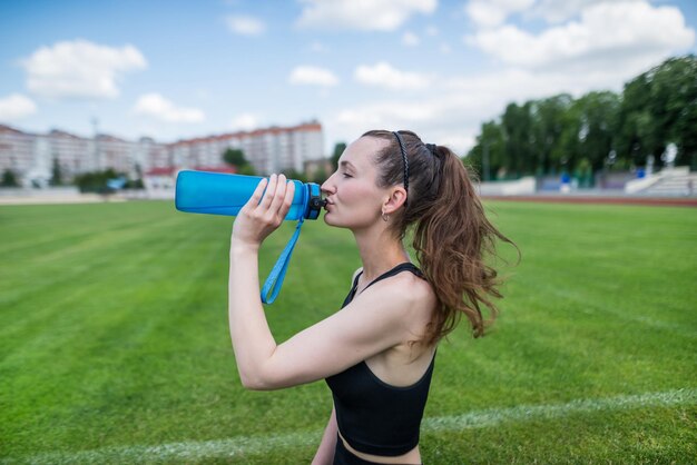 Спортсменка пьет воду на стадионе Тренировка на открытом воздухе