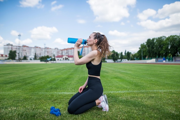 The sportswoman drinks water at the stadium Outdoor workout