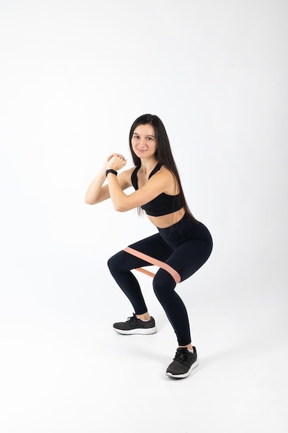 Sportswoman exercising with resistance band on white background Attractive brunette woman in fashionable sportswear exercising Healthy lifestyle sport concept Full length view