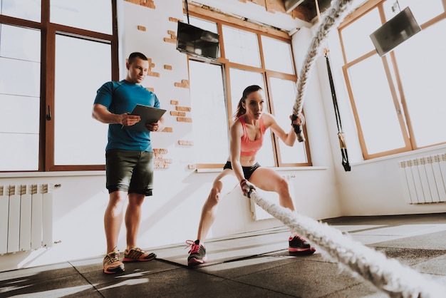 Photo sportswoman is exercises in gym with trainer