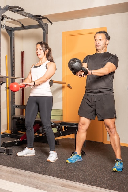 Sportiva e uomo che fanno esercizio di oscillazione con kettlebell in palestra. concetto di esercizi con attrezzature in palestra.