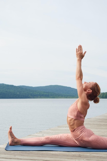 Sportiva in abiti sportivi rosa che praticano yoga in riva al mare