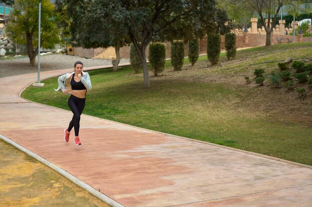 Sportswoman running in the park front view from a distance