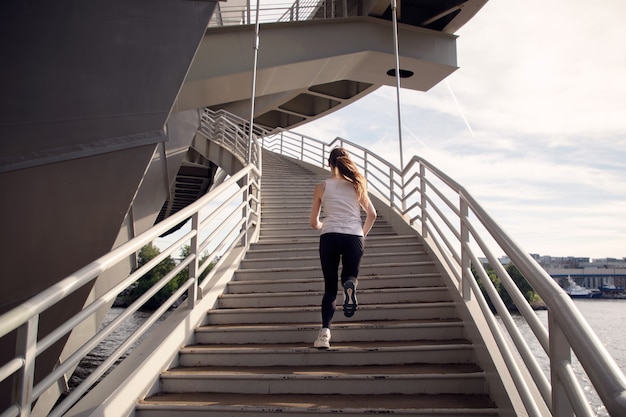 Sportswoman running on the stairs of the bridge