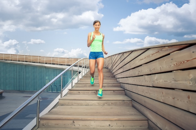 Sportswoman running on wooden stairs under blue cloudy sky