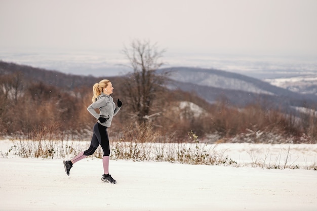 Sportswoman in shape jogging in nature on snow at winter. Cardio exercises, winter sport