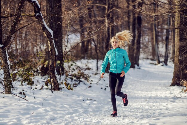 Sportswoman in shape running in forest on snowy path at winter. Healthy lifestyle, winter fitness, outdoor fitness