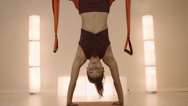Sportswoman standing on hands at yoga class Girl hanging in hammock upside down