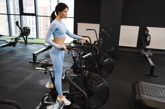 Photo sportswoman training on exercise bike in gym