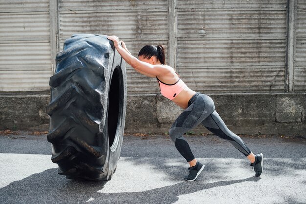 Sportswoman training outdoor weight lifting wheel