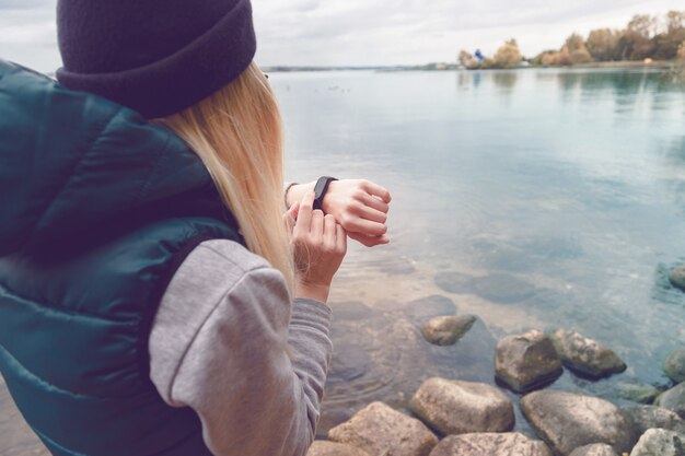 Sportswoman uses an electronic bracelet-pedometer standing on the lake shore. 