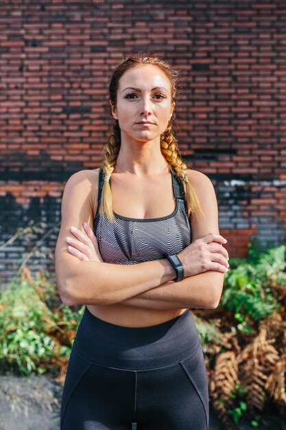 Photo sportswoman with crossed arms looking camera posing in front of a brick wall