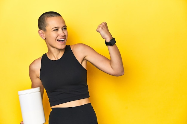 Sportswoman with protein shake yellow studio background raising fist after a victory winner concept