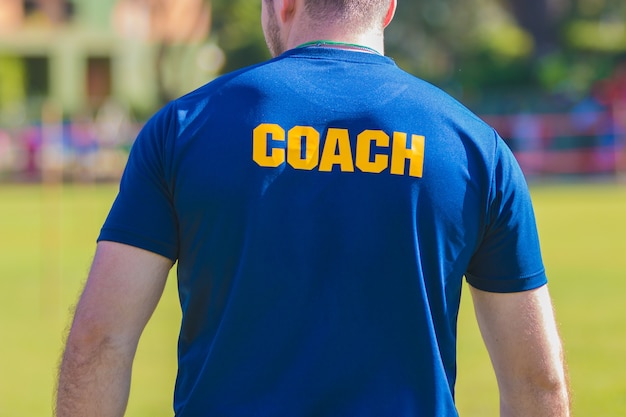 Sporttrainer in blauw shirt met gele coach-tekst op de rug