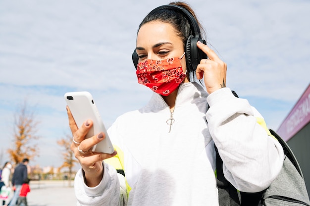 Sportvrouw die met masker aan muziek met hoofdtelefoons en slimme telefoon luistert