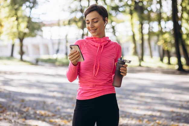 Sportvrouw die telefoon en drinkwater in park gebruikt