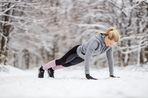 Sportvrouw doet push ups op besneeuwde pad in de natuur in de winter. Winterfitness, sneeuwweer, gezond leven