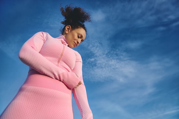 Sportvrouw in sportuniform naar beneden te kijken, staande op de achtergrond van heldere hemel