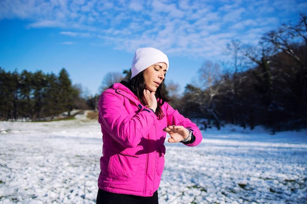 Sportvrouw in trainingskleding winter haar pols meten na het lopen op sneeuw.