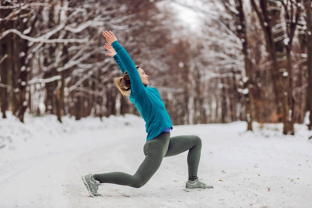 Sportvrouw in warme outfit die yoga-oefeningen doet in het besneeuwde bos. Fitness buitenshuis, sneeuw, kou, winteryoga