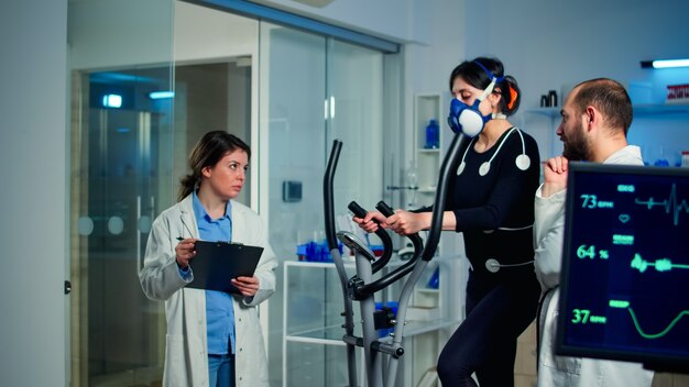 Sportvrouw loopt met masker op crosstrainer met elektroden bevestigd aan lichaam