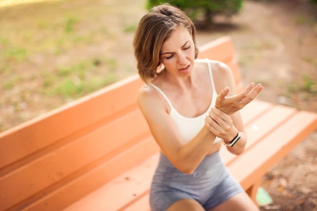 Sportvrouw met armpijn zittend op de bank in het park. Fitness, gezondheidszorg en geneeskunde concept