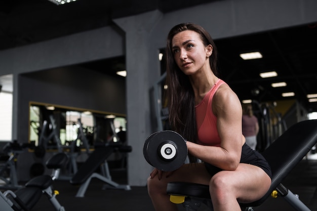 Sportvrouw met gespierde armen die bicepskrullen doen, in de sportschool, kopieer ruimte