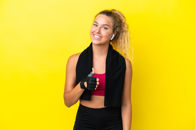 Sportvrouw met handdoek die op gele achtergrond wordt geïsoleerd en een duim omhoog gebaar geeft