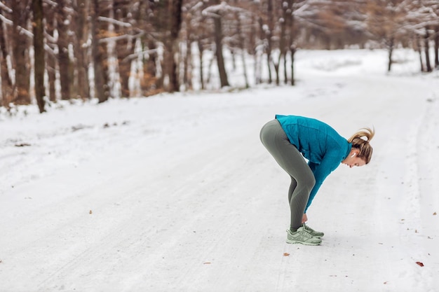 Sportvrouw staande op sneeuw in de natuur in de winter en veter strikken