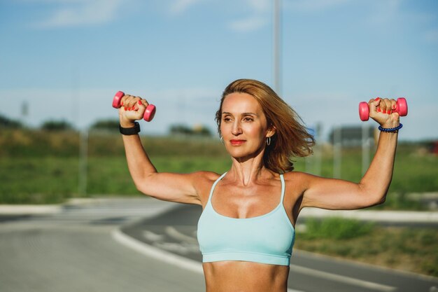 Sportvrouw van middelbare leeftijd die oefeningen met halters doet tijdens de training in de buitenlucht.