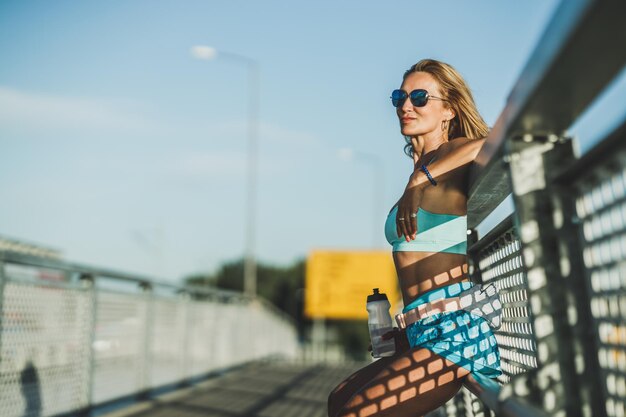 Sportvrouw van middelbare leeftijd die op een brug zit en rust na een zware training.