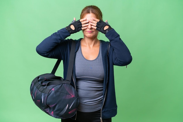 Sportvrouw van middelbare leeftijd met sporttas over geïsoleerde achtergrond die de ogen met de handen bedekt