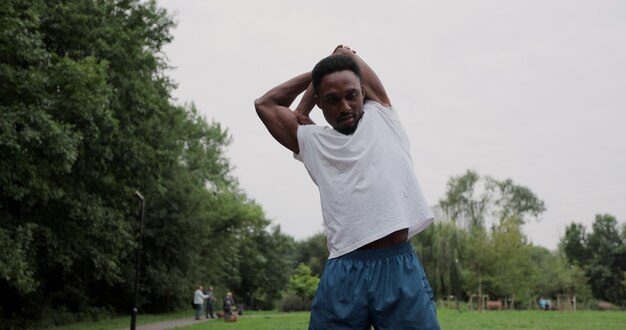 Uomo africano sportivo con riscaldamento allungando le braccia prima di correre nel parco cittadino. sportivo facendo allenamento all'aperto. concetto di stile di vita sano.