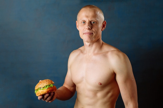 Sporty athlete with hamburger. Unhealthy diet or sport, lifestyle choice. Junk food concept