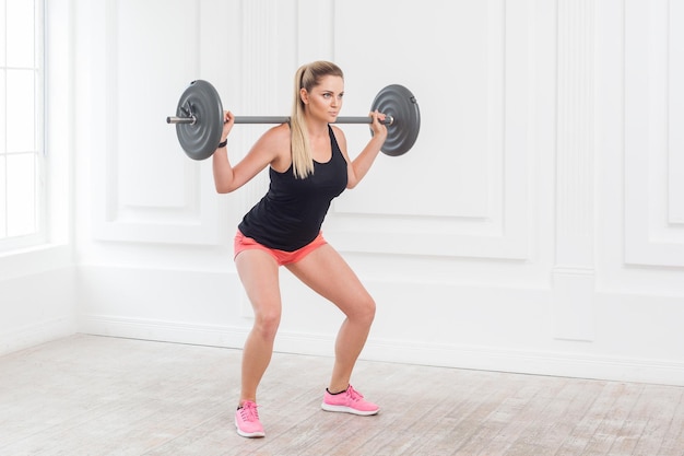 Sporty atletische mooie vrouw doet squats en oefent in de sportschool met de barbell