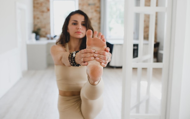 A sporty beautiful girl does yoga exercises standing with her leg stretched out, stretching the spine, shoulders, hamstrings. Close-up of the foot