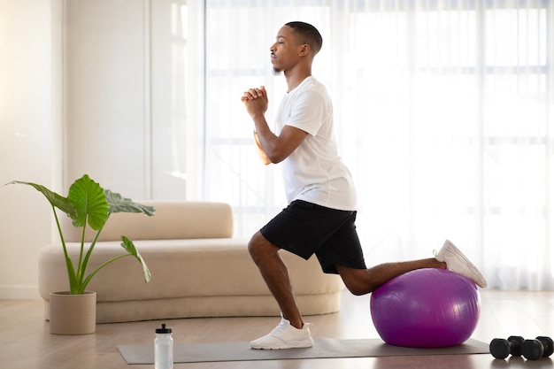 Sporty black guy doing workout at home using fitness ball