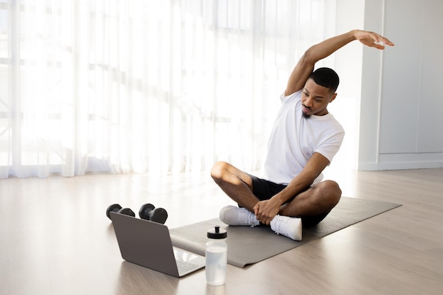 Sporty black guy stretching and watching fitness video on laptop