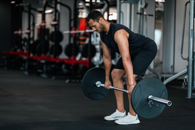 Uomo nero sportivo che solleva bilanciere pesante durante l'allenamento in palestra