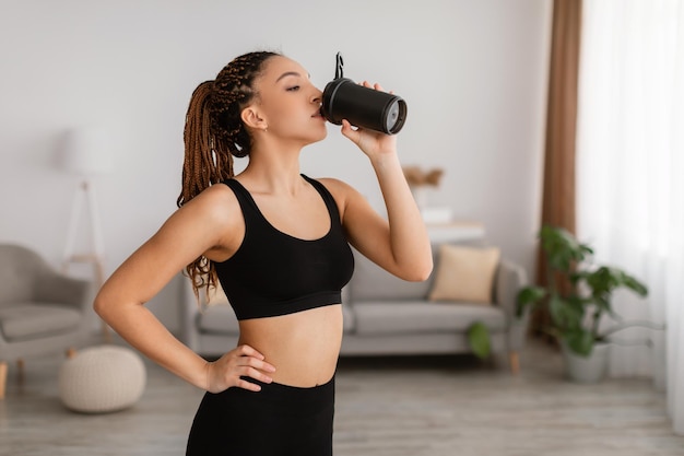 sporty black woman drinking water hydrating during workout at home