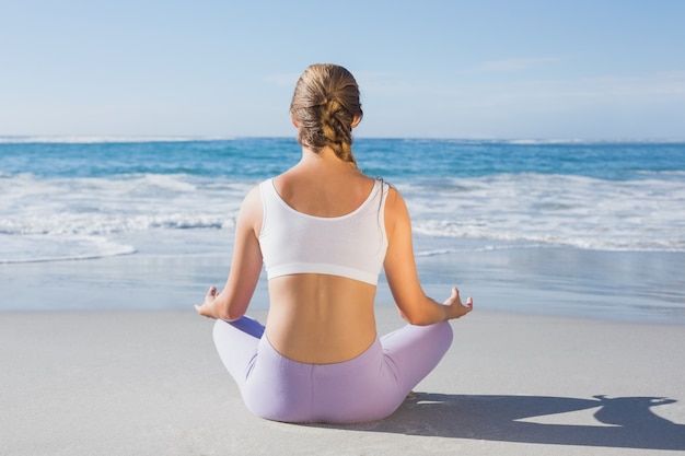 Sporty blonde sitting in lotus pose on the beach