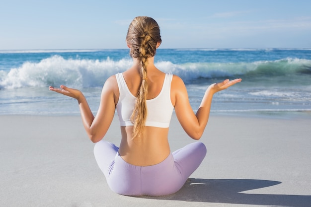 Sporty blonde sitting in lotus pose on the beach