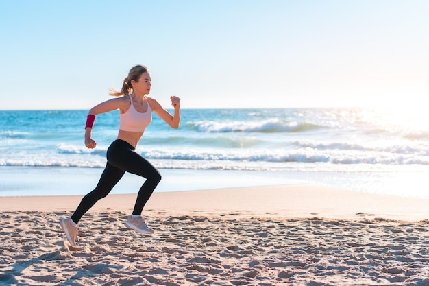 Sporty blonde woman running ocean beach Young caucasian female exercising outdoors running seashore Concept of healthy running and outdoors exercise