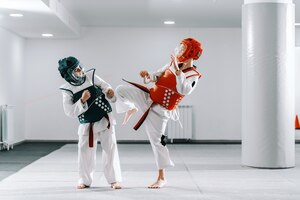 Sporty caucasian boys having taekwondo training in white gym. one boy kicking other.