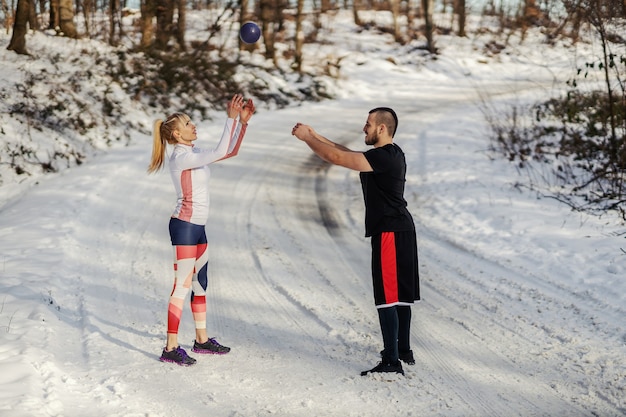 自然の中で雪の中に立って、冬にフィットネスボールでウォームアップ運動をしているスポーティなカップル。