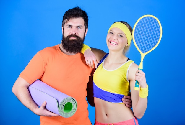 フィットネス マットとテニス ラケットでスポーティなカップル トレーニング スポーツ機器 運動の成功 幸せな女性とひげを生やした男のジムでのトレーニング 強い筋肉と体 最初にいるように遊ぶ