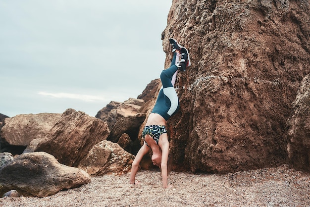 Sporty disabled woman working out outdoors and doing handstand exercise on the beach