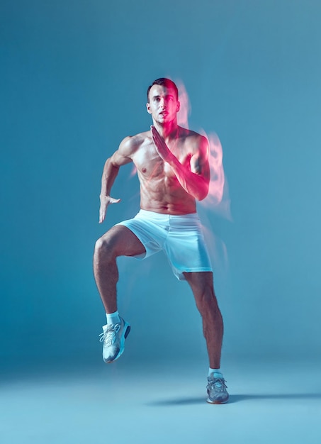 Фото Спортивный энергичный танцор зумбы с обнаженным туловищем, молодой человек в белых шортах на синем
