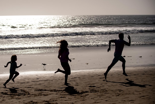 Sporty family father mother and baby son running together child\
with parents run by water along sea sport health and fitness on\
summer
